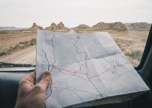 A photo of a man's hand holding a road map while looking out the dashboard at a desert scene.